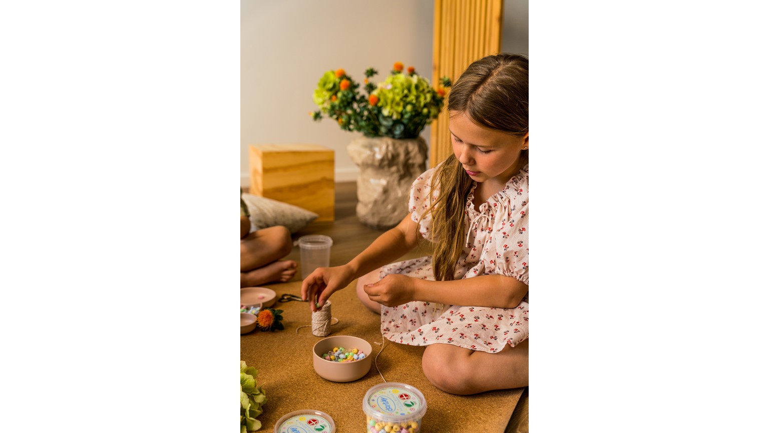 Ved et træbord med en blomstervase arbejdes der med små farverige perler i skåle til håndarbejde